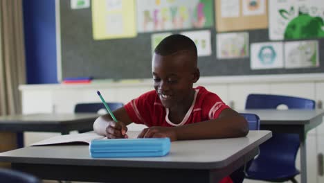 portrait of happy african american schoolboy sitting at classroom, making notes, looking at camera