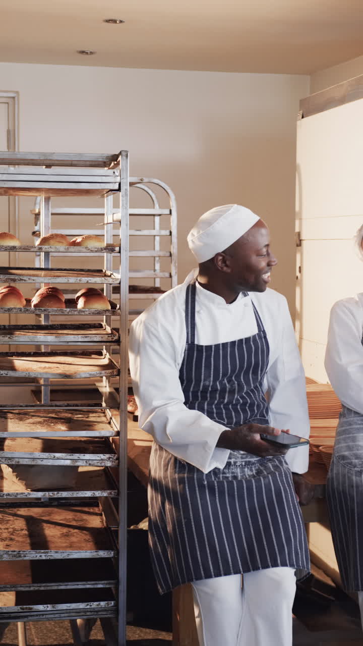 Vídeo vertical de padeiros diversos conversando e usando smartphone na cozinha da padaria, em câmera lenta
