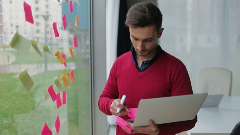 Nachdenklicher-Manager-Mit-Laptop,-Der-Notizen-Am-Fenster-Macht.