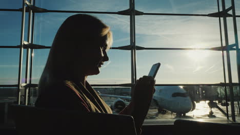 business woman waiting to board her flight at the airport terminal using a smartphone