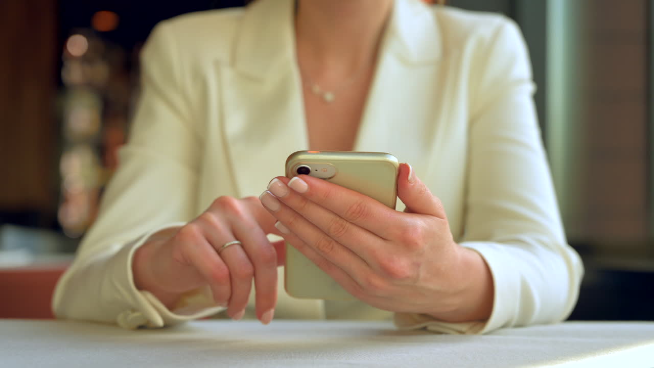 Donna con un blazer bianco che scorre il telefono al tavolo di un ristorante