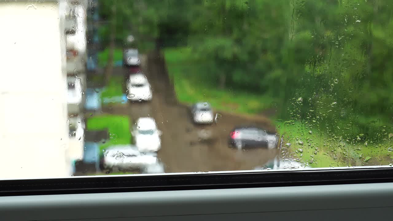 물방울이 창문 유리 위로 흘러내립니다. 도시에서 여름 비가 내립니다. 4k 비디오