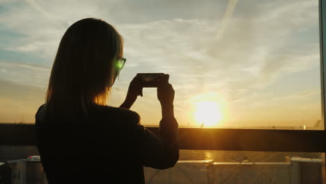 woman takes pictures of an airfield at sunset