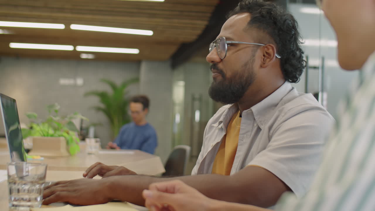 Young Man Using Laptop and Talking with Colleague in Coworking Room