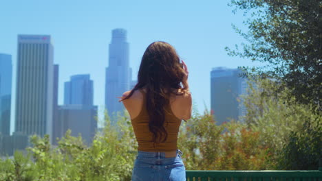 back view brunette tourist making video cityscape standing in green park.