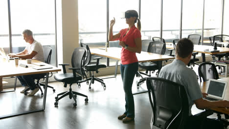 ejecutiva femenina usando auriculares de realidad virtual mientras sus colegas trabajan en el escritorio 4k