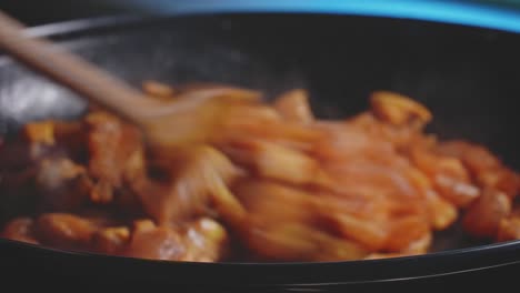 a close up and slightly out of focus shot of sliced chicken breast pieces steamy in a skillet then stirred with a wooden spoon, spreading evenly