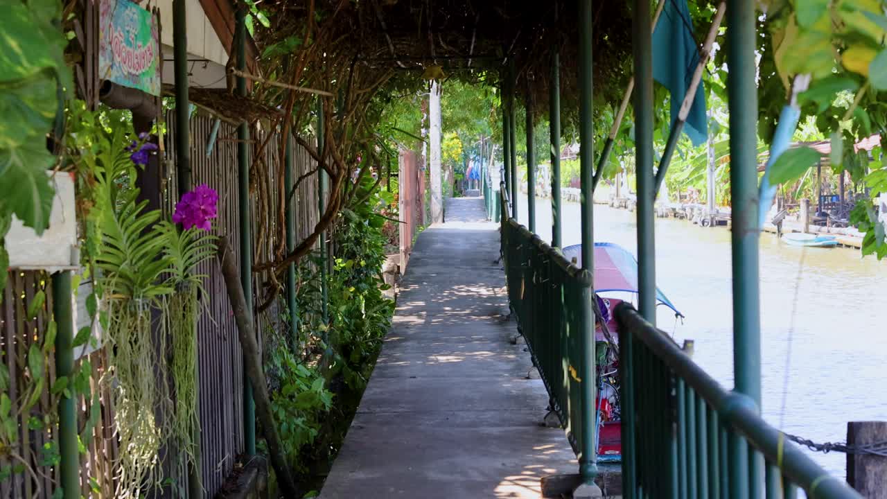A tranquil walkway beside a canal in Bangkok, Thailand, featuring lush greenery and vibrant flowers under soft daylight