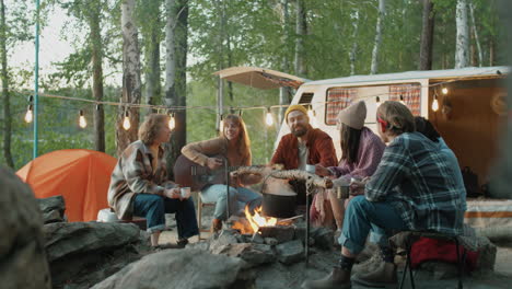 Freunde-Spielen-Gitarre-Und-Stoßen-Am-Lagerfeuer-Mit-Getränken-An