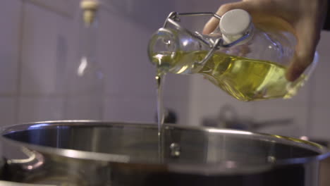 close handheld shot as pouring olive, or sunflower oil from a bottle in to a pot in the kitchen