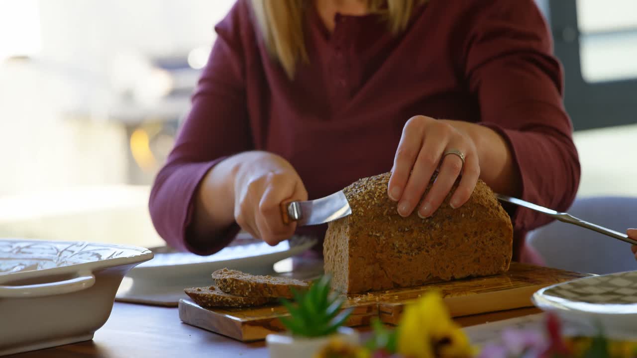 Mid section of woman cutting loaf of bread on dining table 4k