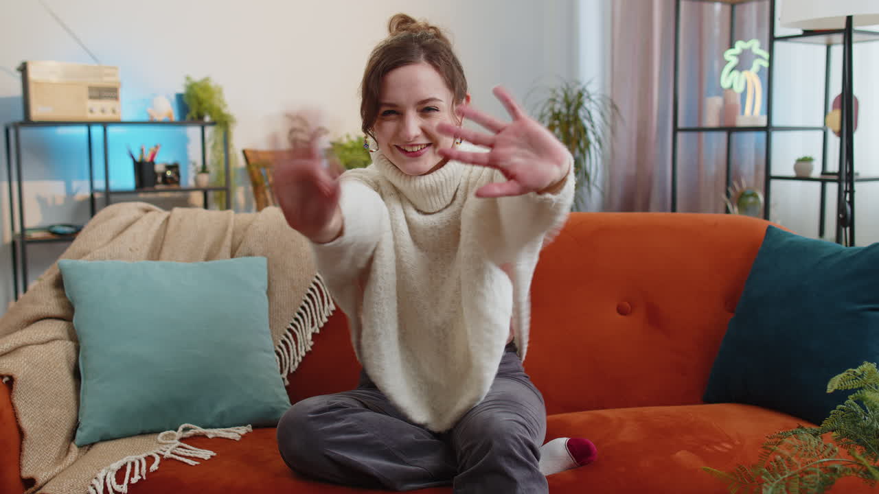 Pretty woman smiling friendly at camera waving hands gesturing hello hi greeting at home on sofa