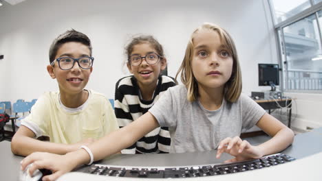chica rubia confiada sentada y escribiendo en el teclado mientras dos compañeros de clase la observan