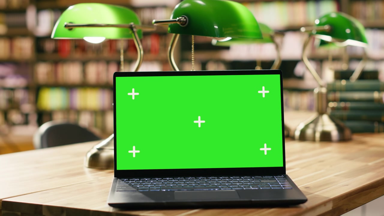Mockup con schermo verde sullo schermo di un laptop aperto in un ambiente accogliente di biblioteca.