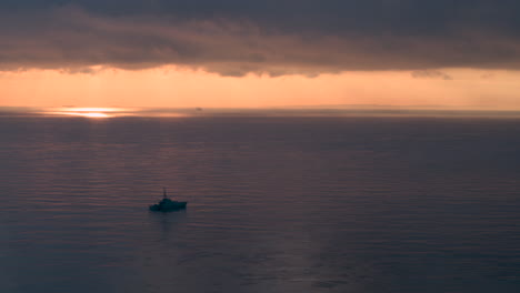 wide aerial view of a royal navy warship sailing on a calm sea at sunrise