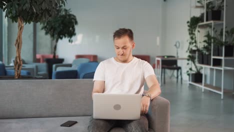 un joven en el vestíbulo del centro de negocios con una computadora portátil espera impacientemente una reunión