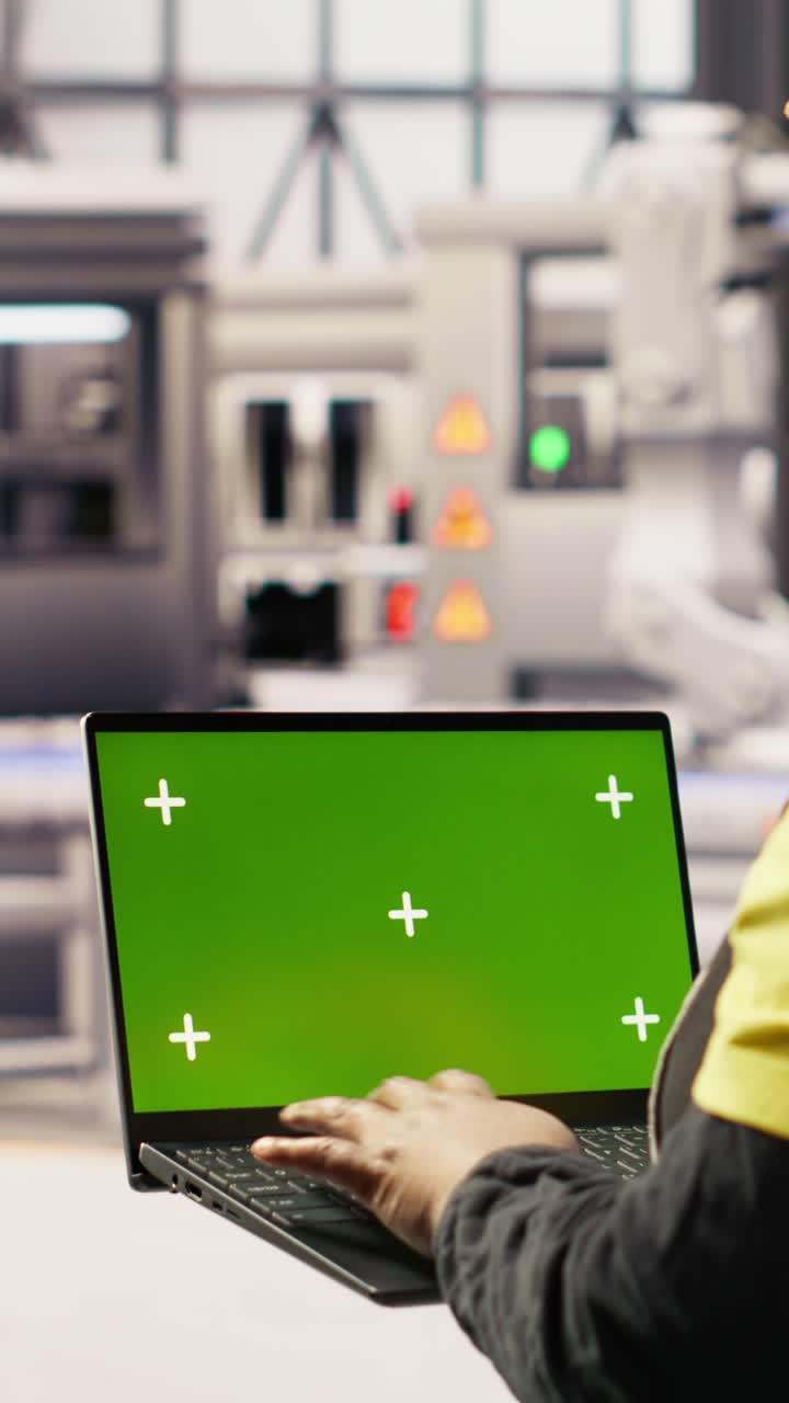 Vertical video Factory engineer typing on green screen laptop, monitoring production lines