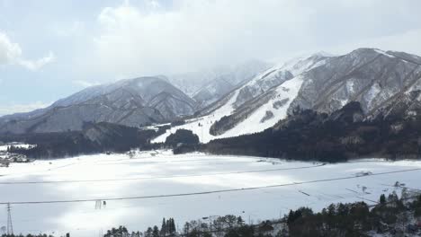 El-Dron-Captura-Con-Gracia-Una-Fascinante-Vista-Aérea-Del-Valle-De-Hakuba-Y-El-Vasto-Campo-Nevado-En-Japón-Durante-El-Invierno,-Mostrando-Un-Paisaje-Cautivador-Adornado-Con-Nieve-Prístina-Y-Bosques-Frondosos.