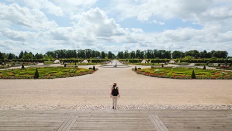 elegant woman descends steps toward symmetrical french garden in summer breeze