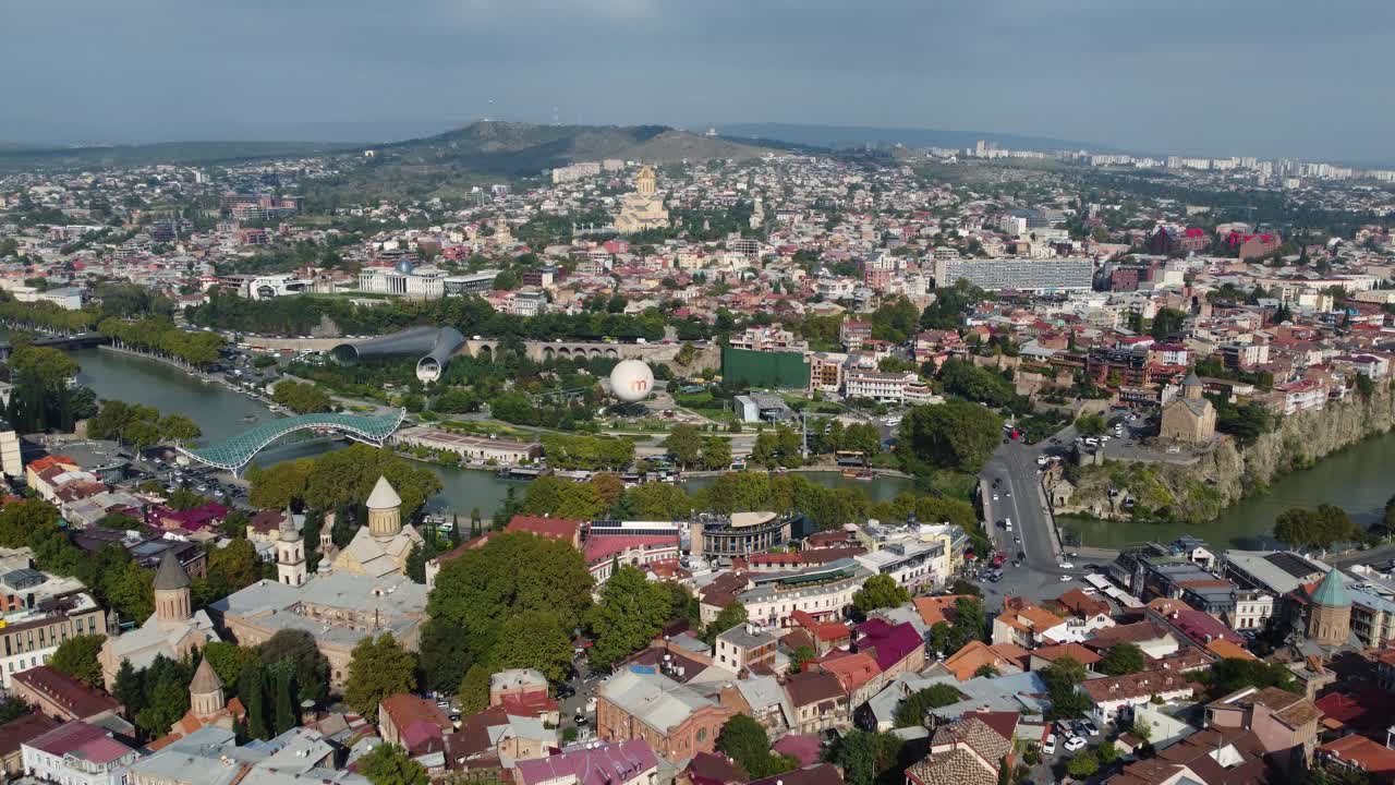 Wide panoramic of Tbilisi city skyline with colorful rooftops under clear blue sky, Narikala Fortress