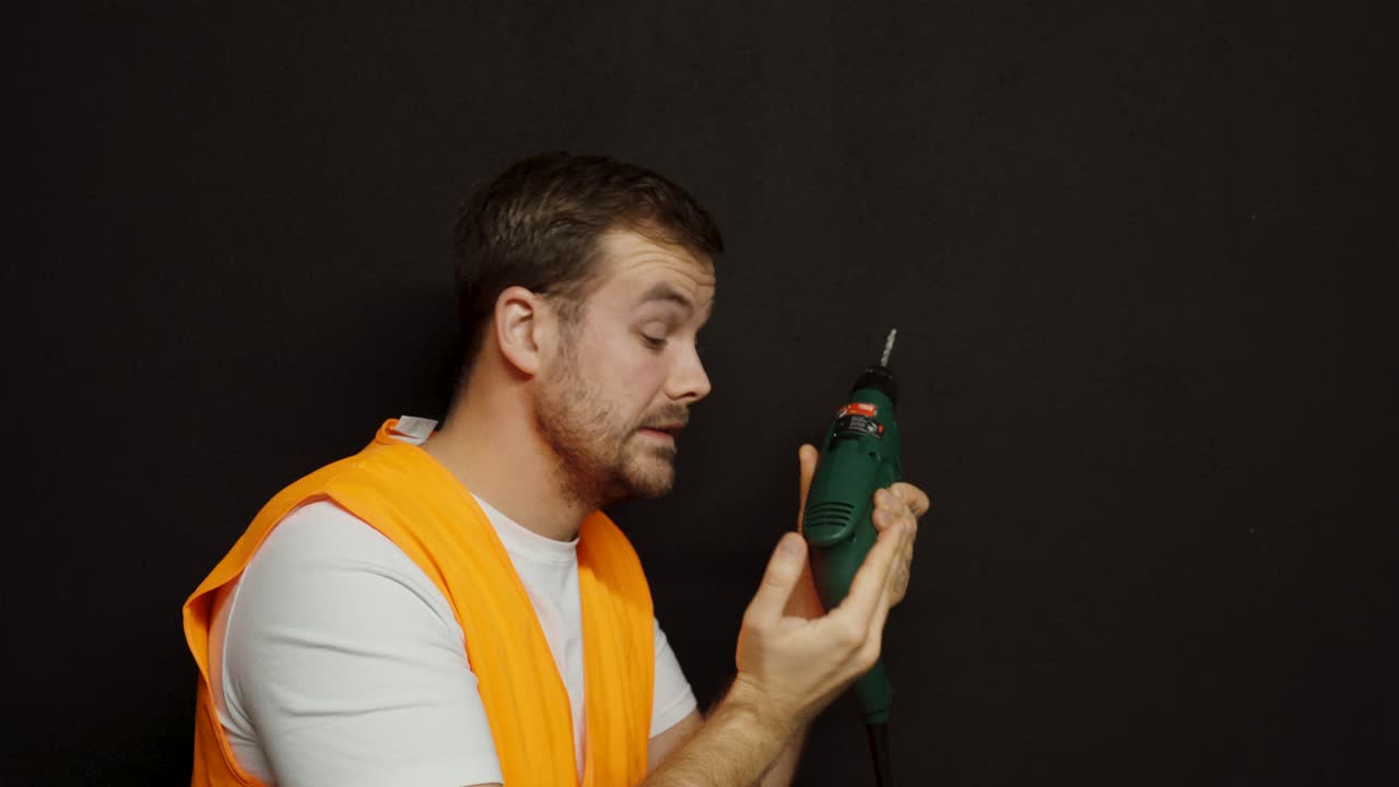 A worker in an orange vest drills without protective eyewear and suddenly gets something in his eye, showing the importance of work safety and personal protection