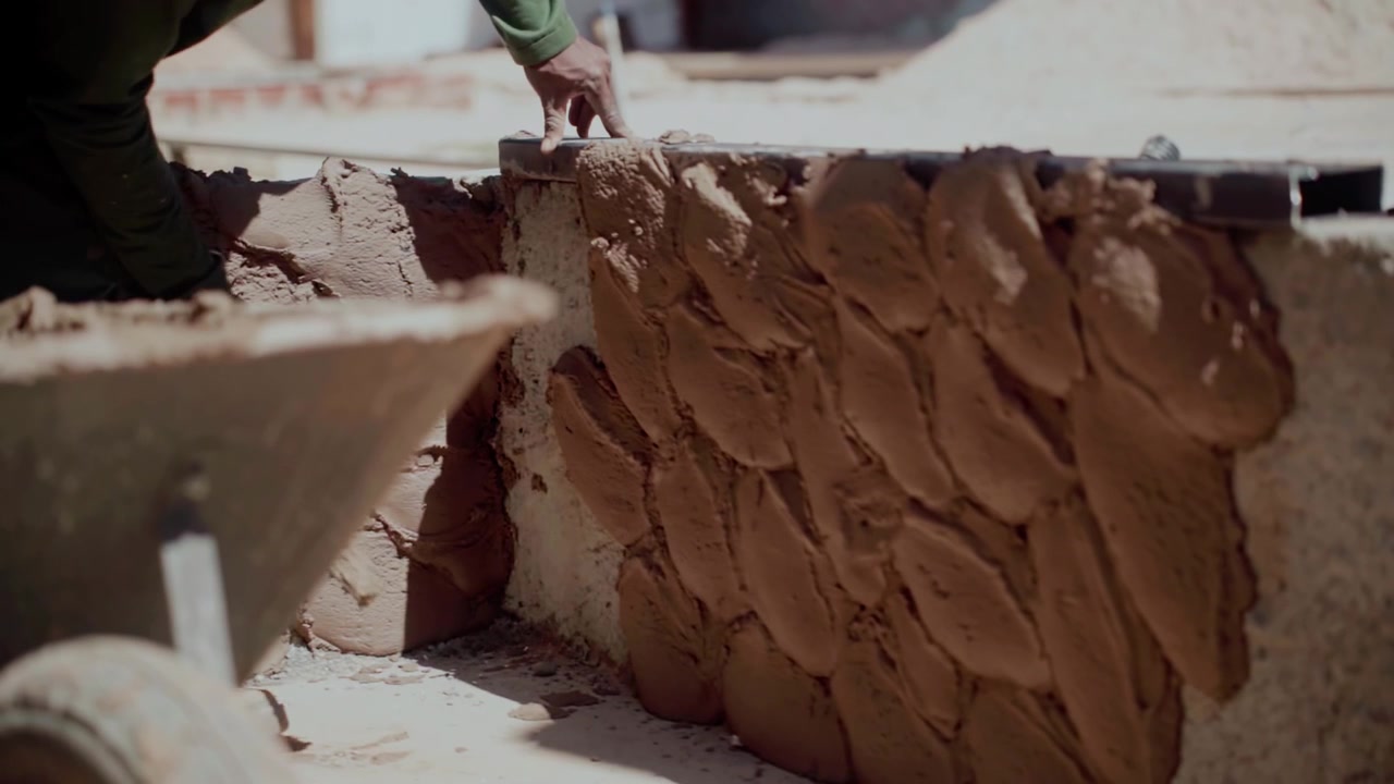 Workers apply cement and sand plaster by hand to a rough masonry wall in Brasilia, Federal District, Brazil, using masonry tools during a slow handheld construction shot.