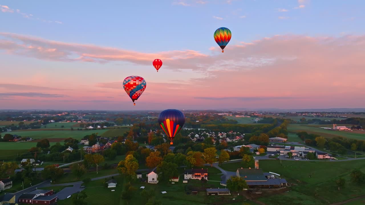 다채로운 뜨거운 공기 풍선은 가을 초기의 부드러운 빛에 목욕 된 조용한 풍경 위에 날아갑니다.