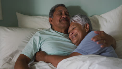 Pareja-De-Raza-Mixta-Senior-Abrazándose-Y-Sonriendo-Acostada-En-La-Cama