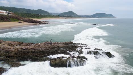 aerial drone shot of a unique rock formation in the ocean off vizag’s coast, surrounded by crashing waves.