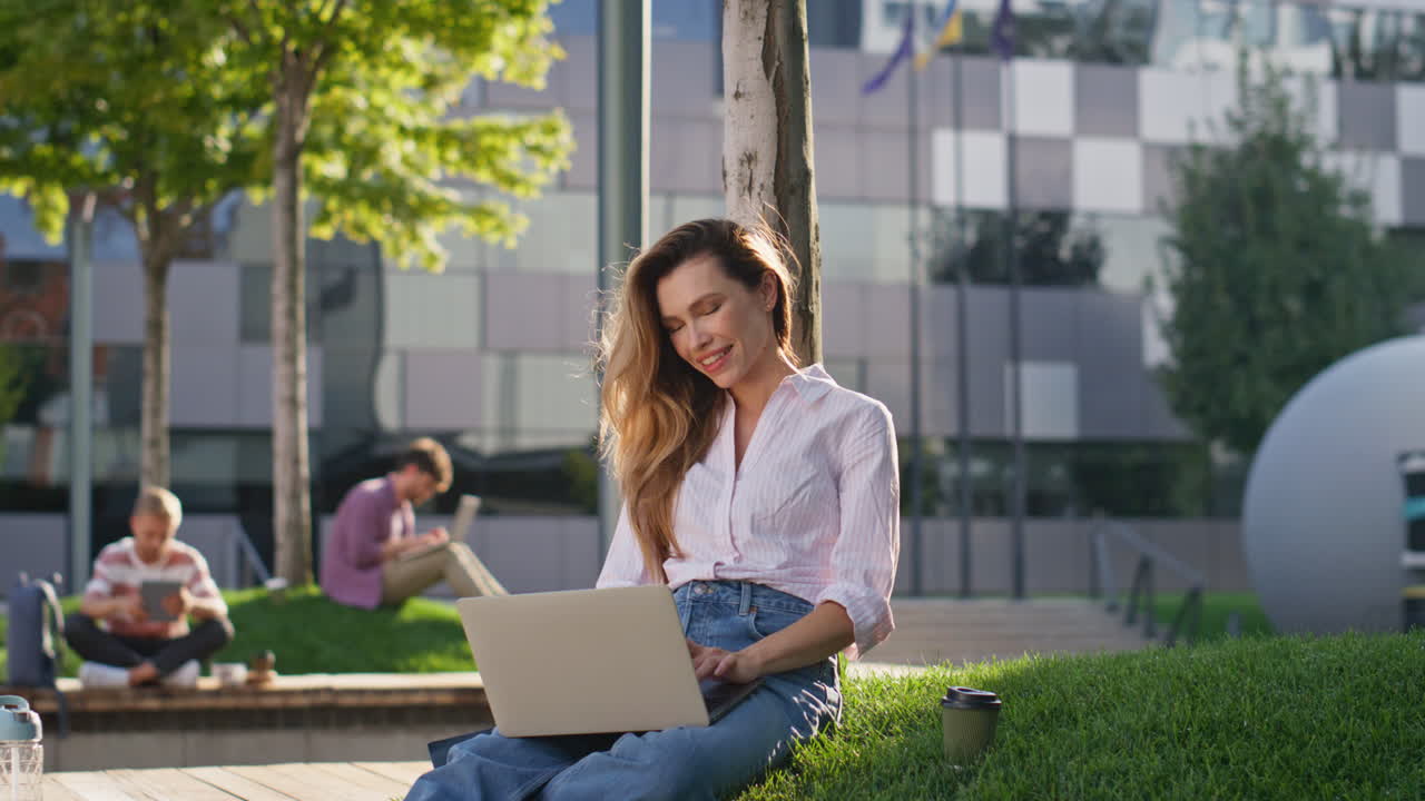 Ragazza freelance che digita al laptop in un parco cittadino. Donna sorridente e ispirata che lavora per strada.