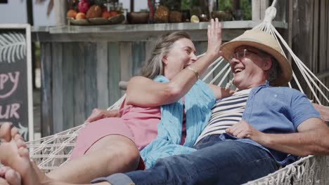 una feliz pareja caucásica senior acostada en una hamaca juntos fuera del bar de la playa, en cámara lenta.