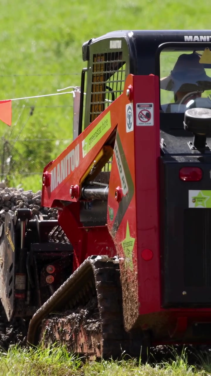 A mini skid steer loader moves gravel on a sunny day at a farm in Byron Bay, Australia