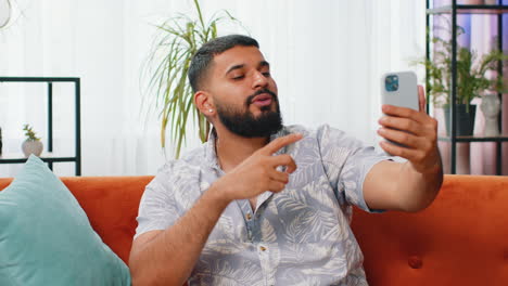 Feliz-Hombre-Indio-Tomando-Selfie-En-Un-Teléfono-Inteligente-Comunicando-Videollamadas-A-Casa-En-Línea-Con-Suscriptores