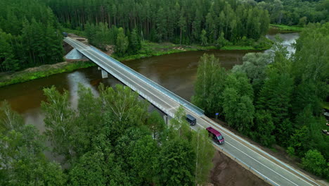 drone flight over a river car bridge in the middle of a large, green forest