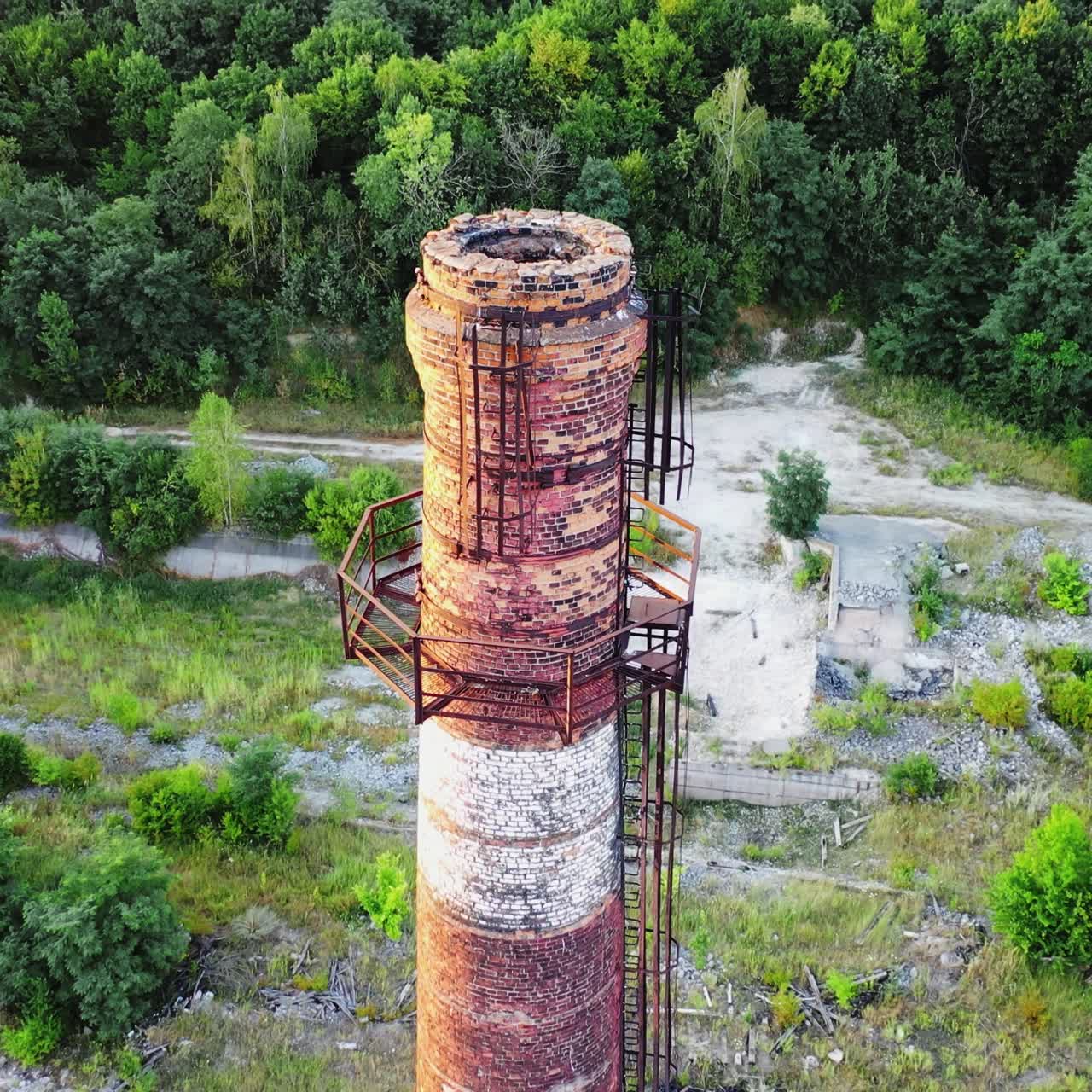 Abandoned pipe among nature. Old brick tower surrounded by green trees in summer. Camera moves top down.