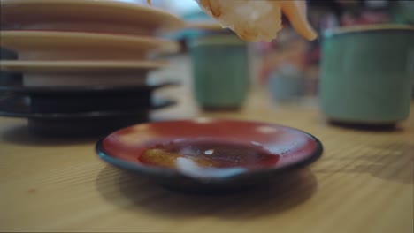 person dipping a piece of salmon toro sushi in the soy sauce using wooden chopsticks with a stack of empty saucer on the background at the sushi restaurant in numazu, shizuoka, japan