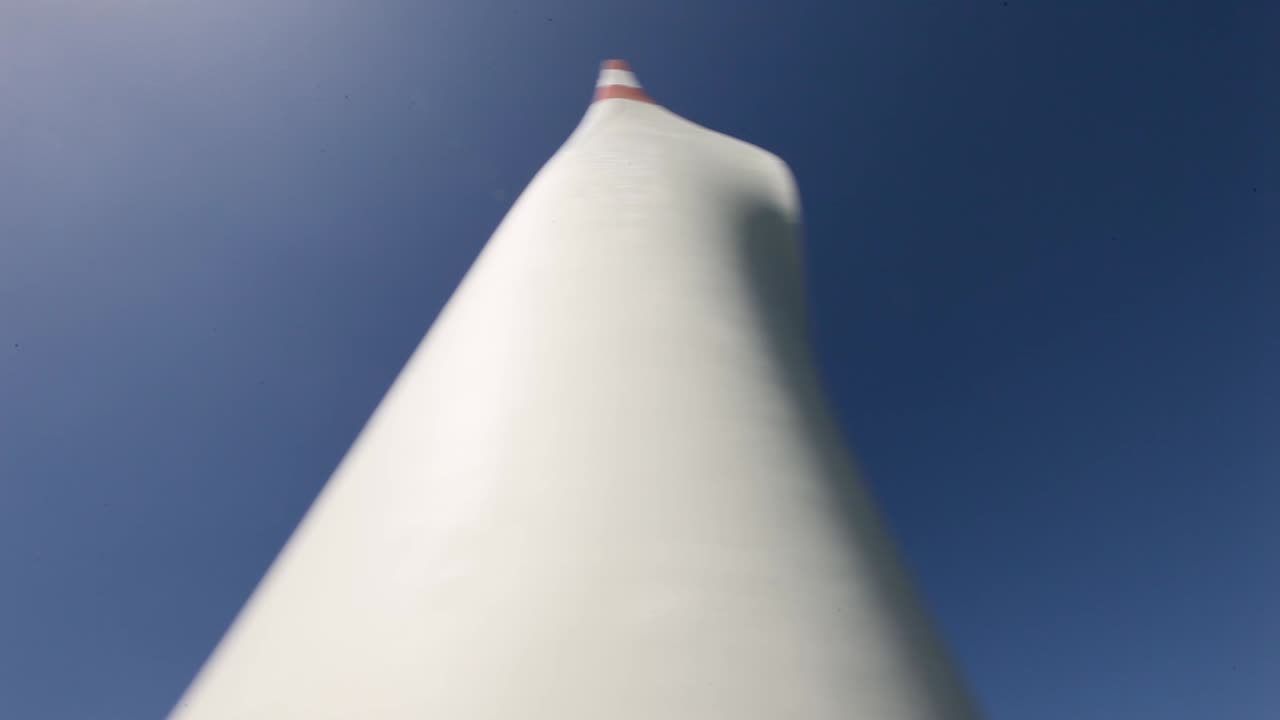 Looking up at a towering wind turbine blade against a clear blue sky