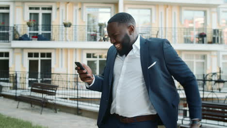 cheerful afro man receiving good news on the phone outside