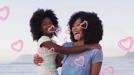 animation of happy african american mother and daughter embracing at beach over hearts