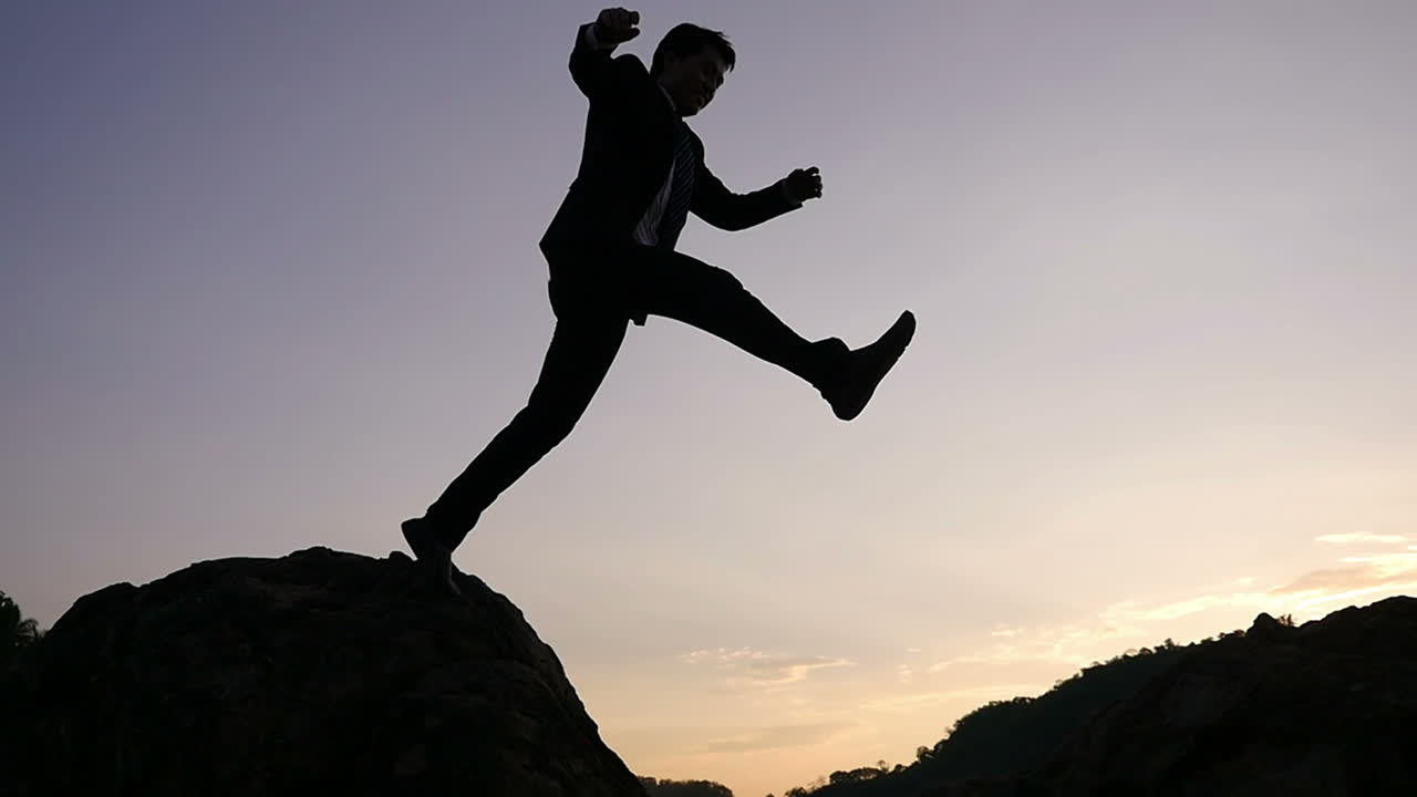 Businessman Jumping Over Rocks at Sunset
