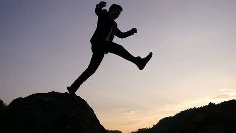 businessman jumping over rocks at sunset