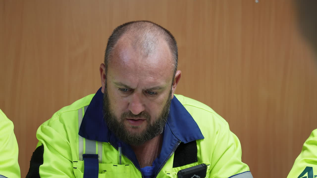 Worker in safety jacket looking down during a meeting