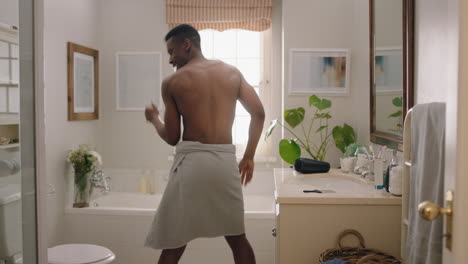 happy african american man dancing shirtless in bathroom looking in mirror having fun morning routine getting ready enjoying positive self image doing silly dance celebrating success