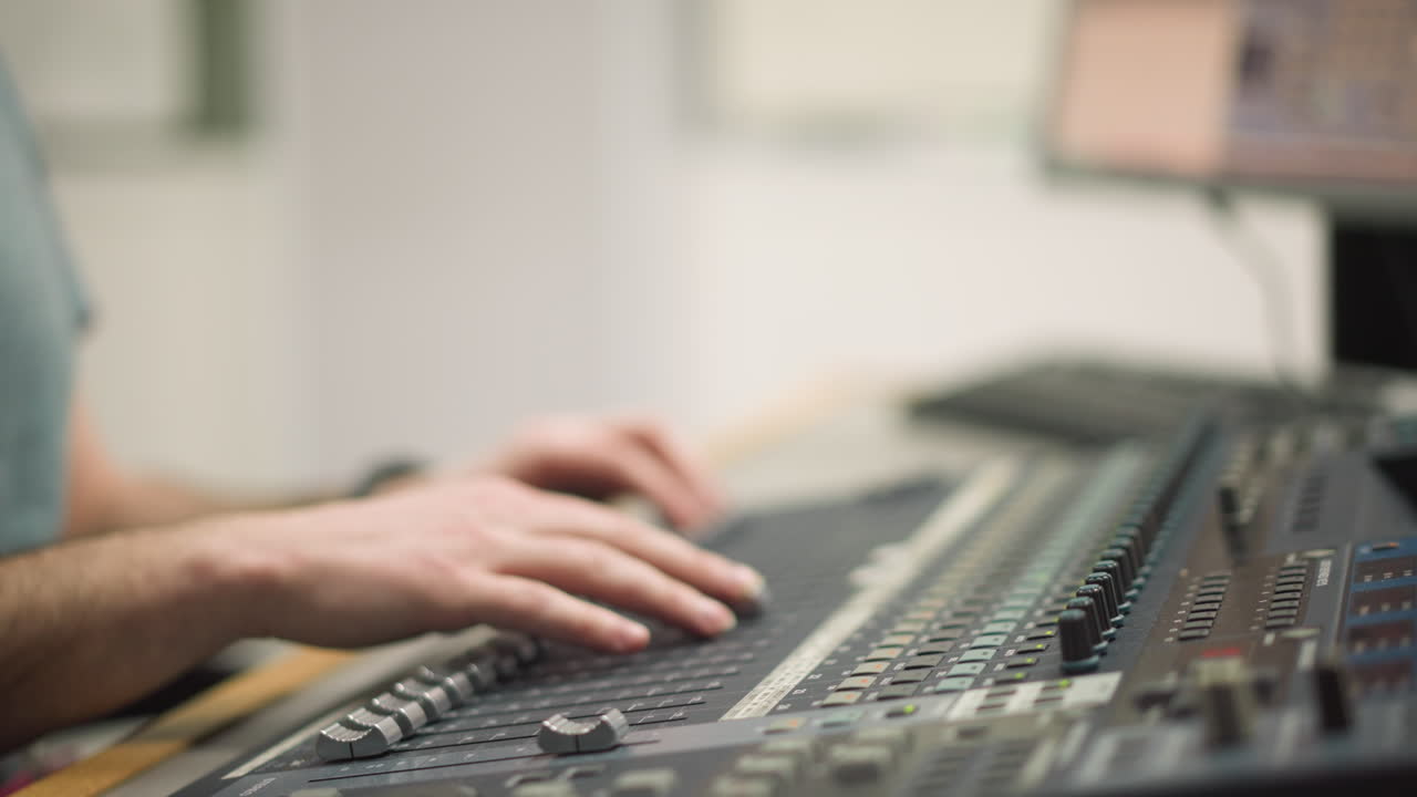 Close-up of hands adjusting faders on audio mixing desk in broadcast studio. Focus on sound engineer controlling audio levels and making adjustments during live broadcast