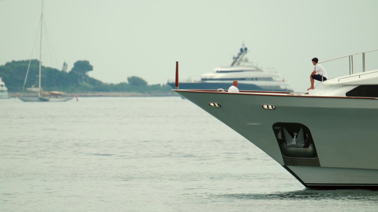 Due uomini che si godono una crociera su un grande yacht a motore privato nell'oceano con un'altra barca a vela sullo sfondo.