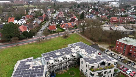 solar panels on roof of apartment block during cold winter day. parking cars and green grass. neighborhood with single family houses and modern architectures. wide shot.