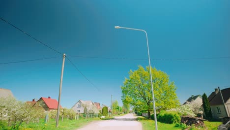 Slow-motion-FPV-footage-of-a-Baltic-village-landscape,-capturing-a-dirt-road,-a-traditional-house,-and-a-tree