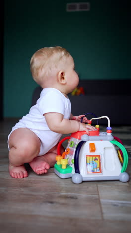 beautiful baby boy sits on the floor of his room. child has a toy beside him but looks aside. vertical video.