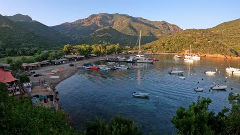 zoom in of girolata beach and small harbor with moored boats and people on vacation in summer season at sunset