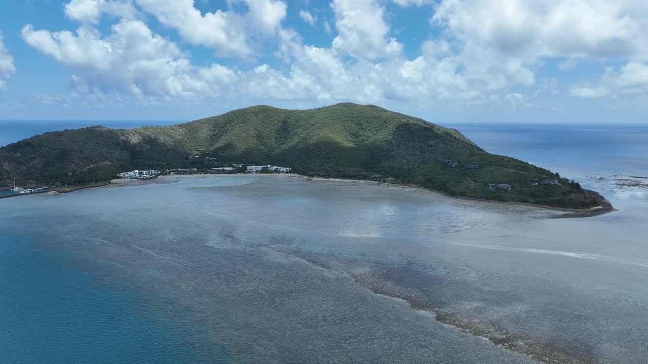 Lenta ripresa in avvicinamento con drone di giorno, che si muove verso la cresta verde dell'isola di Hayman, sopra le basse piane della baia e i motivi della barriera corallina, Whitsundays, Queensland, Australia.